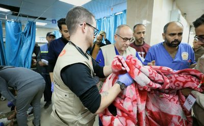 A photo of a ward in a hospital, a group of medical staff stand holding a blanket.