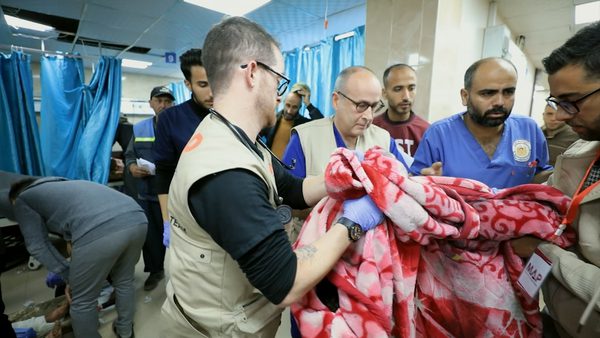 A photo of a ward in a hospital, a group of medical staff stand holding a blanket.