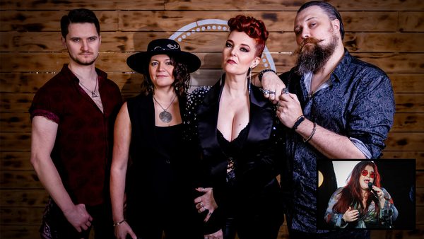 Group of four people standing in front of a wooden background. From left to right: one person in a short-sleeved shirt, another wearing a hat and necklace, a third dressed in black with visible cleavage, and a fourth with a beard in a patterned shirt. An inset at the bottom right shows a red-haired individual singing into a microphone..