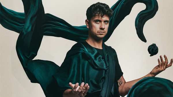 Person in a dark outfit, surrounded by floating dark green fabric, hands positioned as if controlling the fabric.
