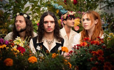 Four people wearing light-coloured shirts surrounded by vibrant flowers and greenery in a garden setting.