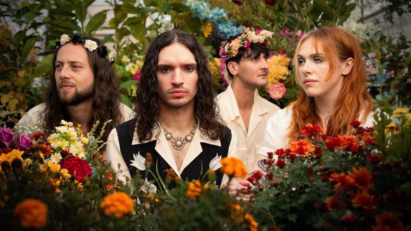 Four people wearing light-coloured shirts surrounded by vibrant flowers and greenery in a garden setting.