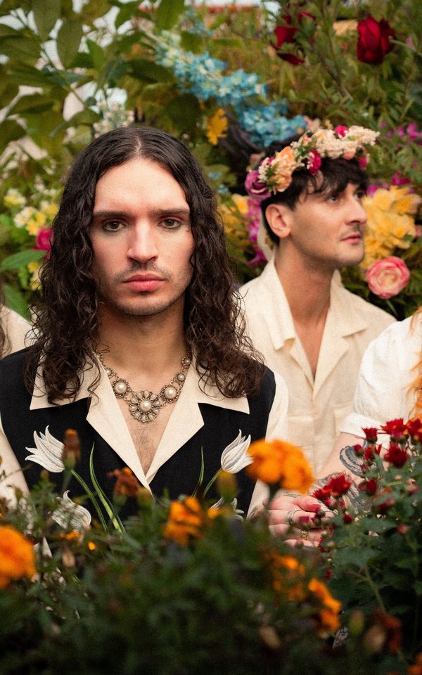 Four people wearing light-coloured shirts surrounded by vibrant flowers and greenery in a garden setting.