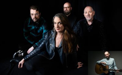Four people posing against a dark background; the person in front wears a black leather jacket and has long hair, while the others behind wear a green plaid shirt and dark clothing. An inset at the bottom right shows someone sitting with an acoustic guitar.