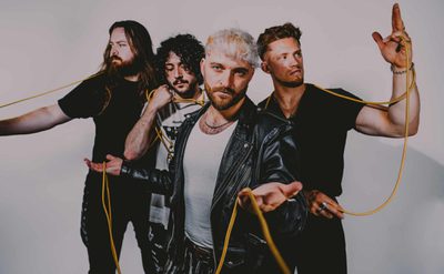 A photo of four people standing with a yellow cable wrapped around them, each person looks in a different direction, the band member at the front of the photo is looking straight ahead at the camera.