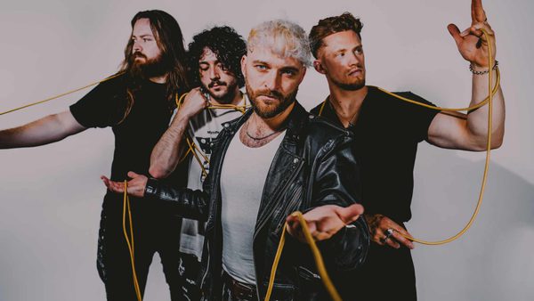 A photo of four people standing with a yellow cable wrapped around them, each person looks in a different direction, the band member at the front of the photo is looking straight ahead at the camera.