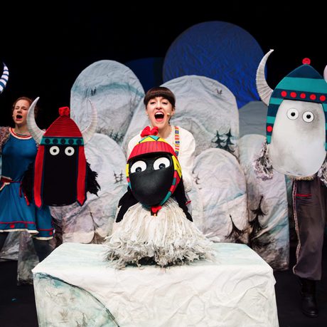 Stage scene with whimsical animal-like characters in colorful costumes, set against a snowy backdrop.