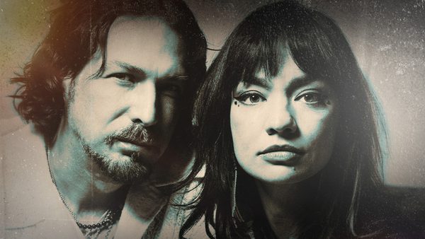 Two people standing in front of a textured, vintage-style background.