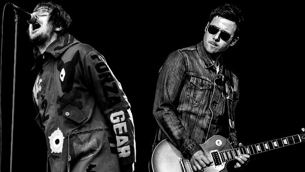 A black and white photo of two performers. One is singing in to a microphone and the second is playing an electric guitar.