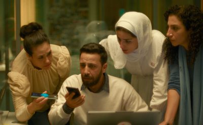 Four people gathered around a laptop in an office setting, engaged in a collaborative discussion.
