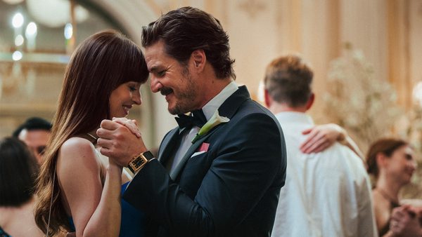 A couple dancing closely in a formal setting, with the man in a dark suit and bow tie and the woman in a blue dress. Other guests are seen dancing and socializing in an ornate venue.