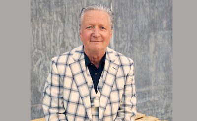 Person in a cream plaid suit sitting against a textured grey wall.