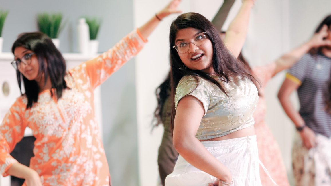 Four people participating in a dance or exercise activity with one arm raised and the other bent.