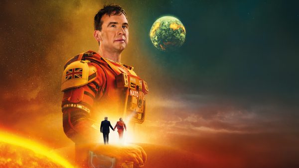 A person in red‑orange futuristic armour stands in a glowing sci‑fi landscape, with a large planet overhead and two smaller figures walking hand‑in‑hand toward the bright horizon.